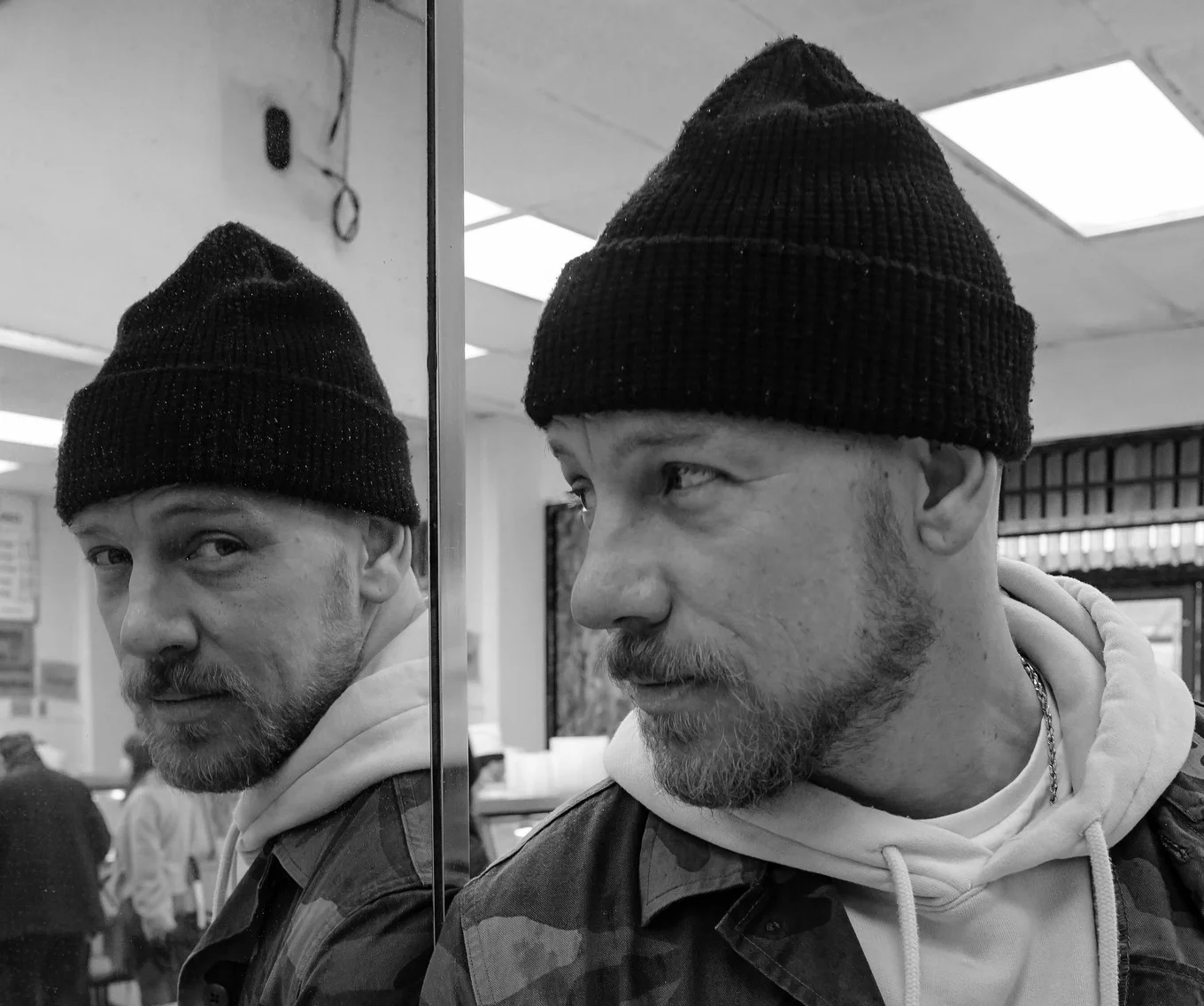 BBTX in a black beanie beside a mirror, with his reflection looking at the camera