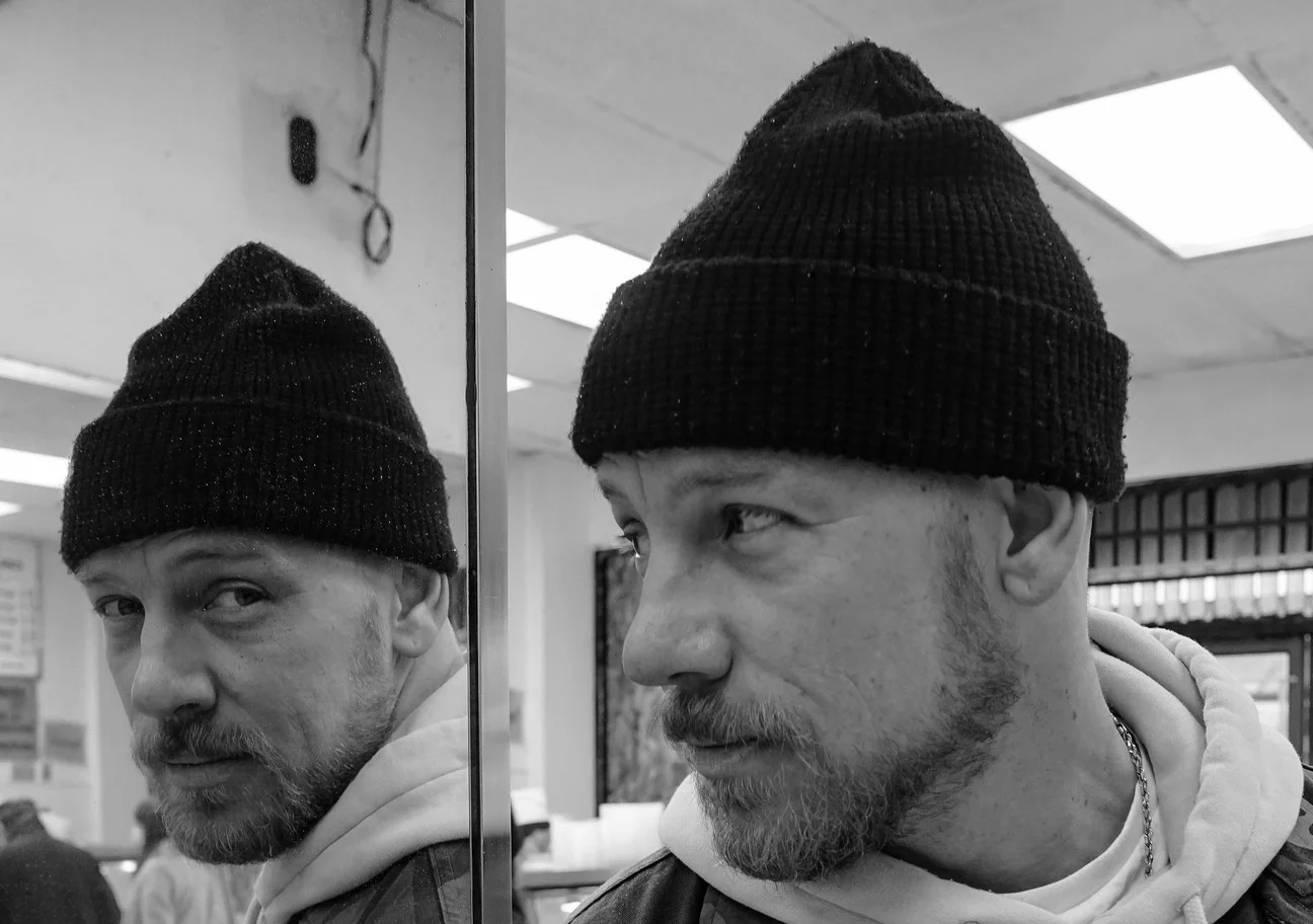 BBTX in a black beanie beside a mirror, with his reflection looking at the camera